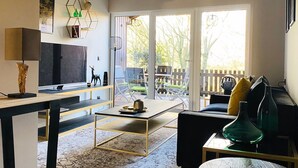 Una sala moderna con un televisor de pantalla plana, una mesa de centro y un sofá. Una ventana grande ofrece vistas al exterior.