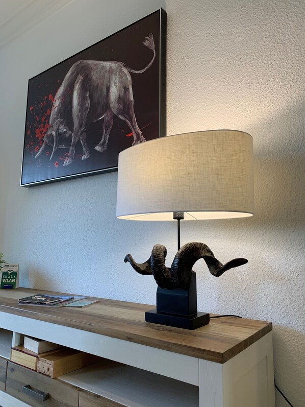 Una habitación moderna con una mesa consola de madera, una lámpara con pantalla texturizada y una obra de arte enmarcada de un toro en la pared.