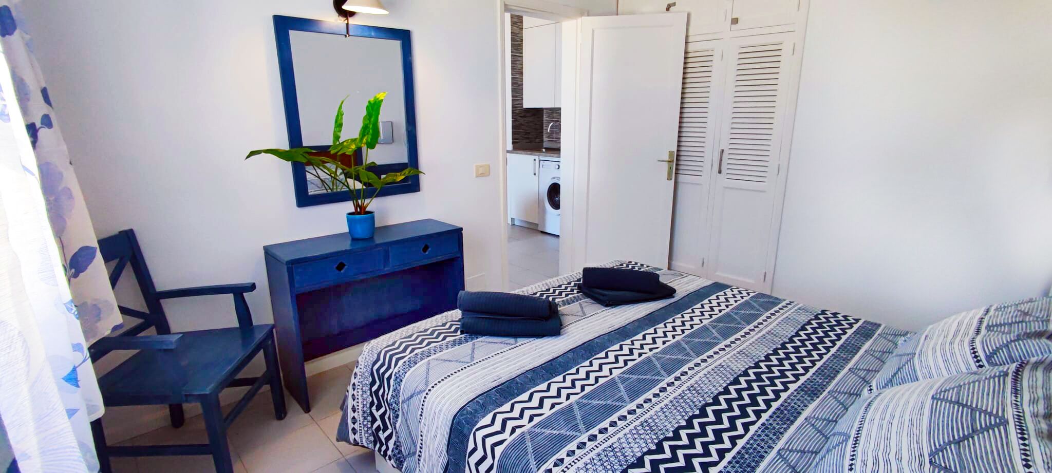 Une chambre à coucher avec un lit, un bureau, une chaise, une armoire et une machine à laver à l’arrière-plan.