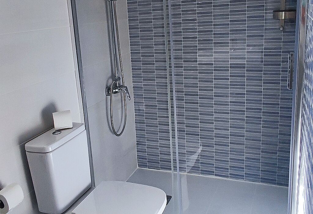 A modern bathroom with a toilet, a paper towel dispenser, and a shower with a glass door.