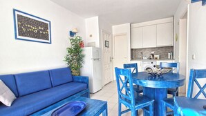 A compact living space with a blue sofa, a dining table with blue chairs, a kitchen area, and a potted plant. - Sunny and comfy appartment in a residencial development near the sea (Puerto del Carmen, Tias)