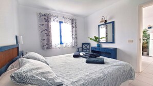 A bedroom with a bed, a dresser, a mirror, a potted plant, and a window with curtains. - Sunny and comfy appartment in a residencial development near the sea (Puerto del Carmen, Tias)
