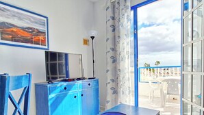 A room with a blue cabinet, a television on top, a table with a blue plate, and a view of the sea through an open door. - Sunny and comfy appartment in a residencial development near the sea (Puerto del Carmen, Tias)