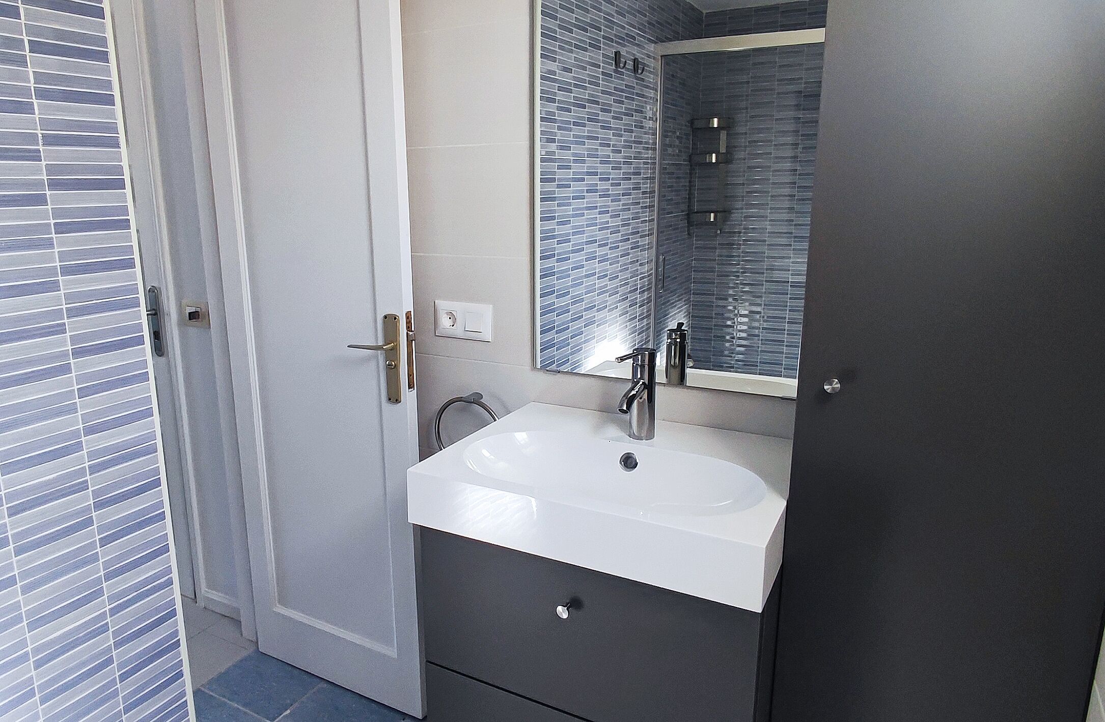 Een badkamer met een wit wastafel, een spiegel en een douchehoek.