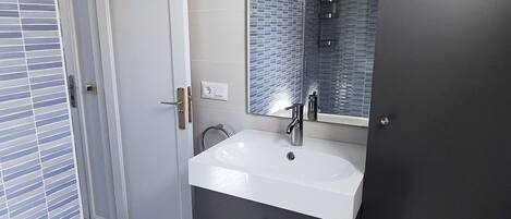 Een badkamer met een wit wastafel, een spiegel en een douchehoek.