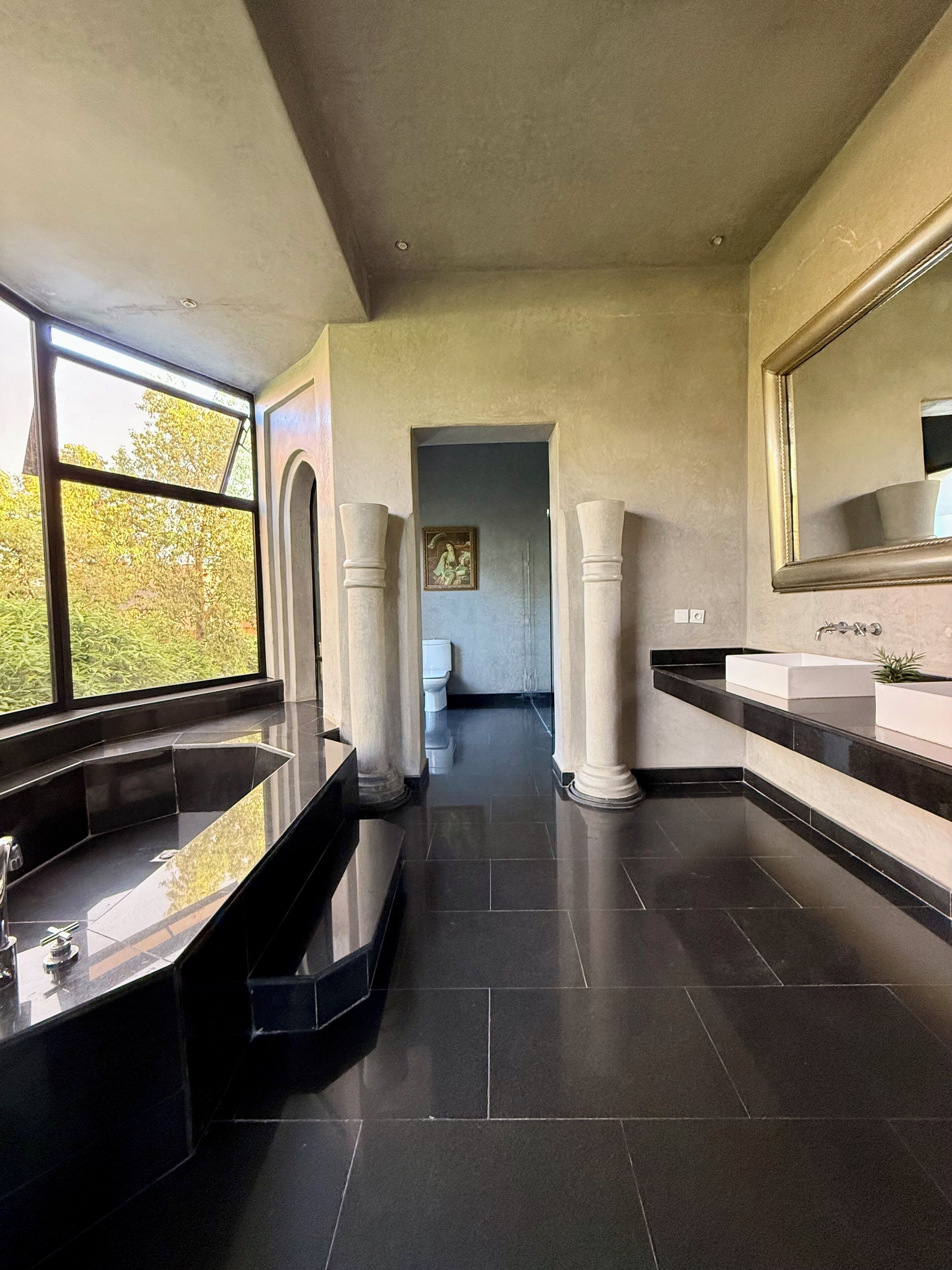 A modern bathroom with a large bathtub, a vanity with a mirror, and a view of the outdoors through large windows.