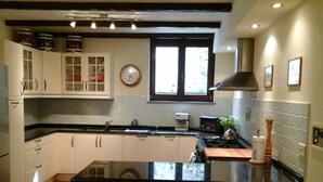 A kitchen with white cabinets, a black countertop, a stove, a sink, and a window with blinds. -  Villa with own pool, mountain village with restaurant and shop. North of Lucca (Pieve Fosciana)
