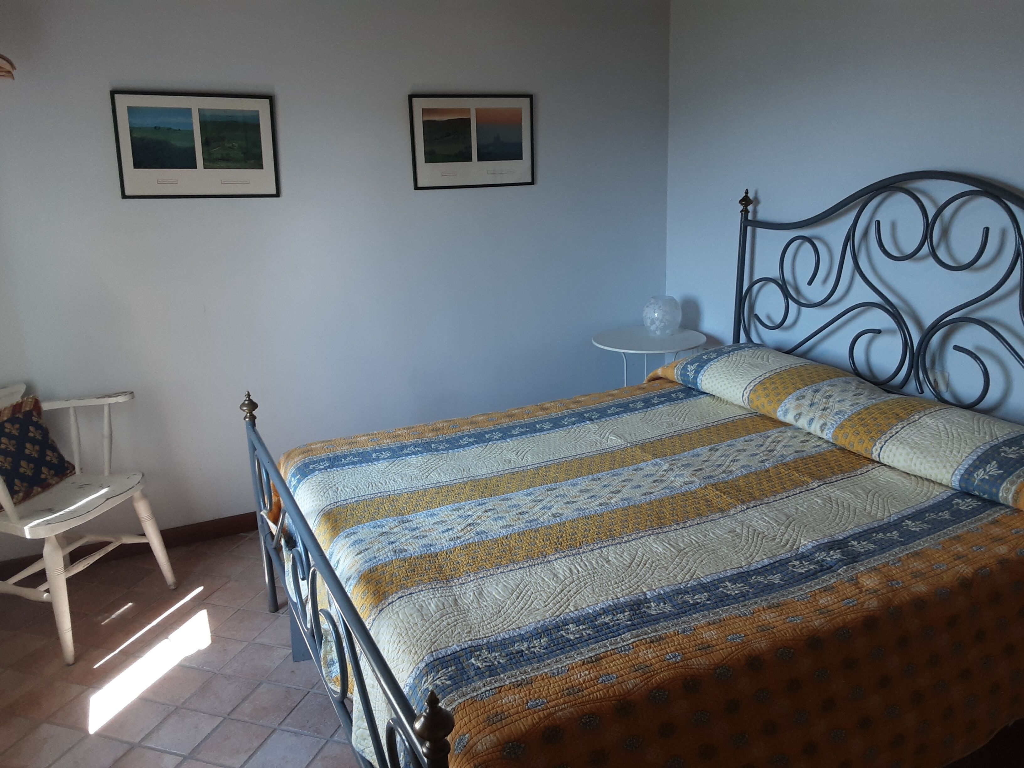 A bedroom with a bed, a chair, a small table, and two framed pictures on the wall.