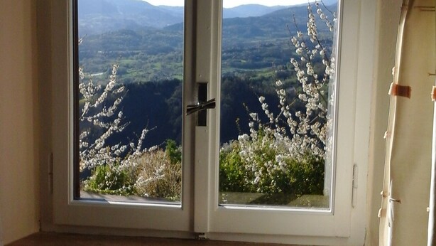 A room with a large sliding glass door leading to a scenic view of mountains and flowering trees. -  Villa with own pool, mountain village with restaurant and shop. North of Lucca (Pieve Fosciana)