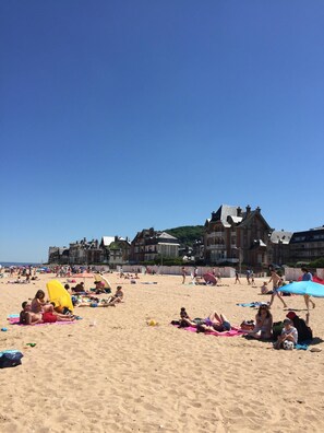 A beach with people sunbathing and playing, a large yellow umbrella, and historic buildings in the background.