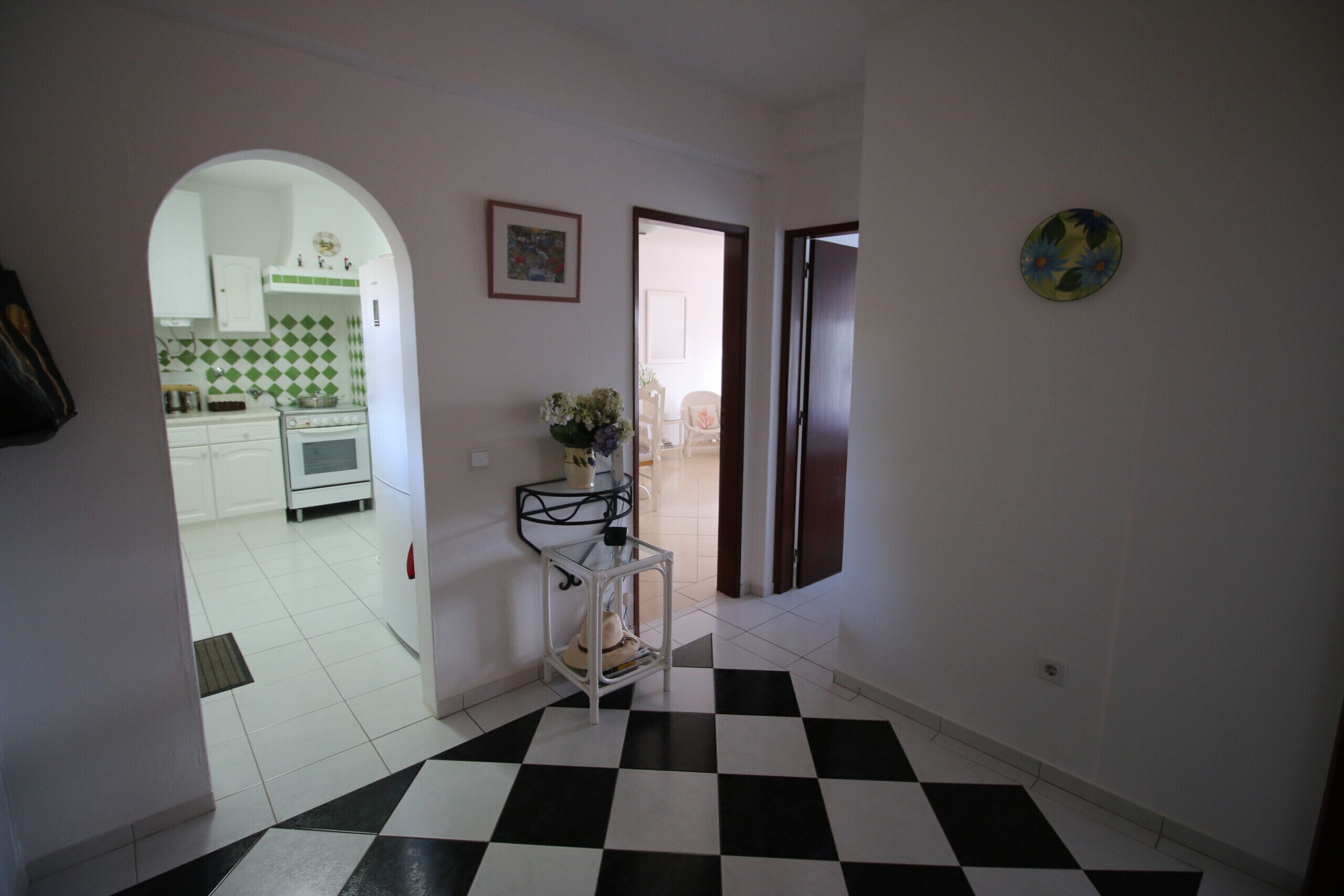 Un pasillo con piso a cuadros, una puerta blanca y una cocina visible a través de un arco.