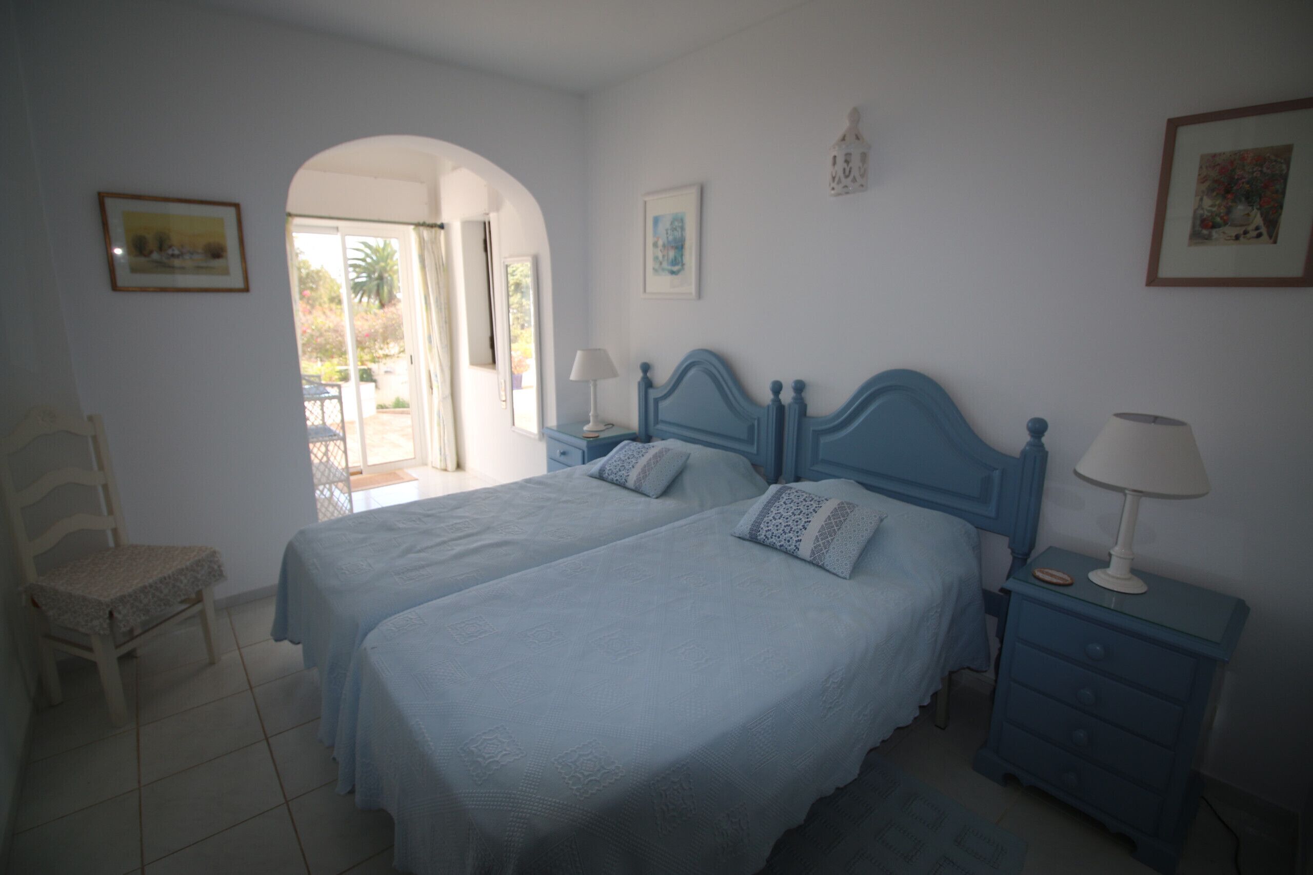 Une chambre avec deux lits, une chaise, une table de chevet avec une lampe et une porte donnant sur un espace extérieur.