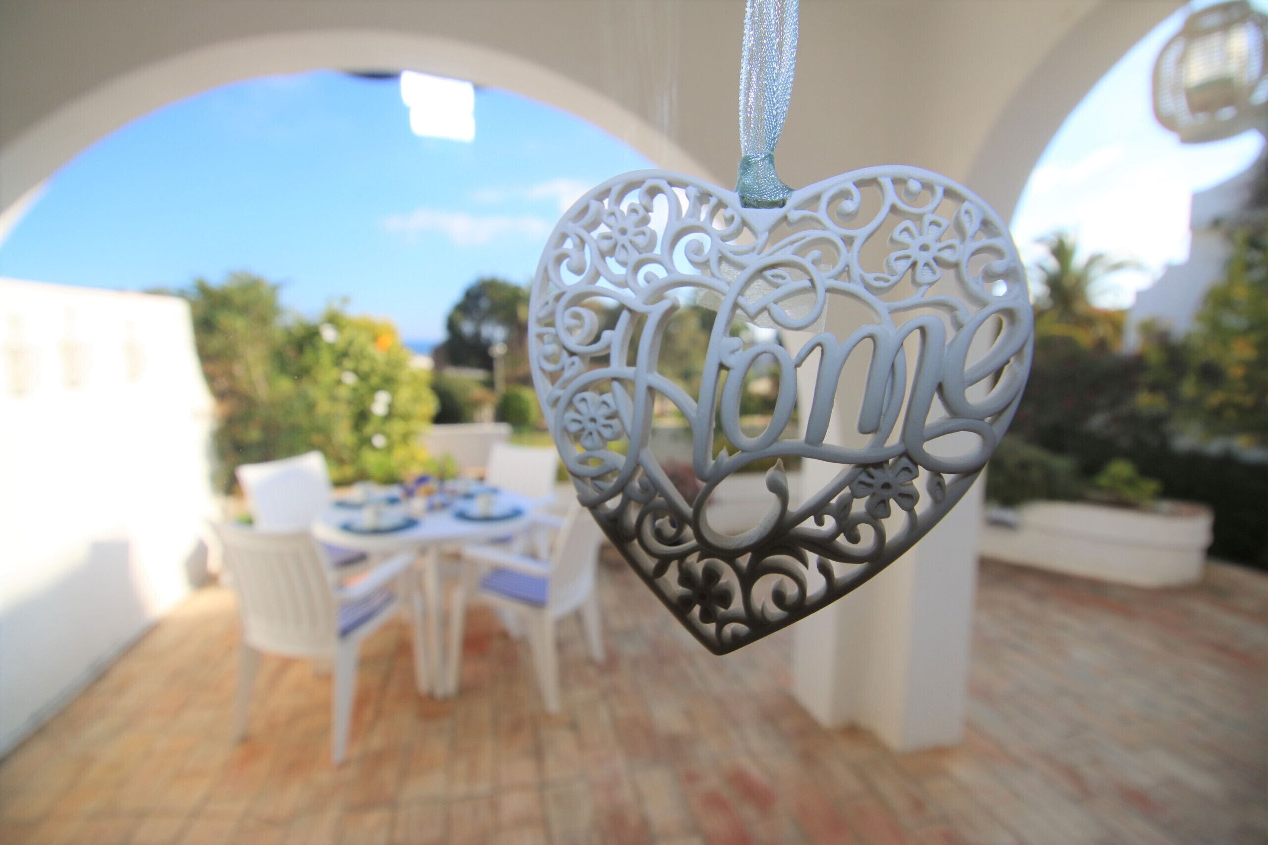 A heart-shaped ornament with 'Home' written on it, hanging in a white archway.