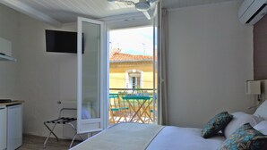 A hotel room with a bed, a small kitchenette, a TV mounted on the wall, and a balcony with a table and chairs. - Hôtel du Golfe (Balaruc-les-Bains)