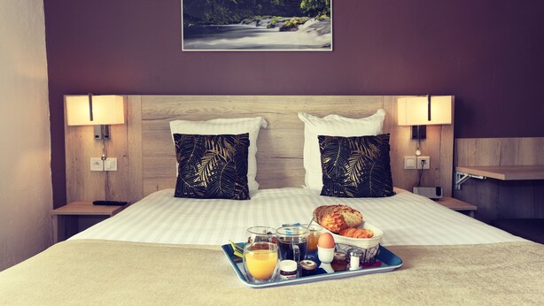 A neatly made bed with a tray of breakfast items, two pillows with a leaf pattern, and a framed picture of a forest on the wall. - Hôtel du Golfe (Balaruc-les-Bains)