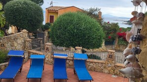 Un espace piscine avec quatre chaises longues bleues, un mur en pierre et une vue sur un bâtiment doté d’une porte rouge.
