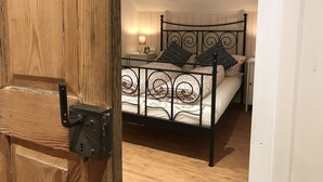 A bedroom with a skylight, a bed with patterned bedding, a bedside table with a lamp, and a wooden door. - Klein Bullerbü im Alpbachtal Tegernsee (Tegernsee)