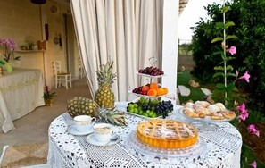 A table set outdoors with a fruit platter, pastries, and a cake. - B&B Giardino Isabella (Palagiano)
