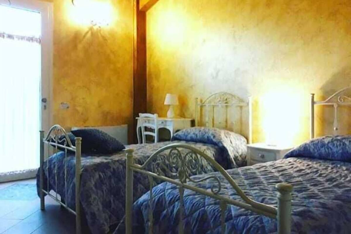 Quarto com duas camas, uma mesinha com abajur e uma porta.