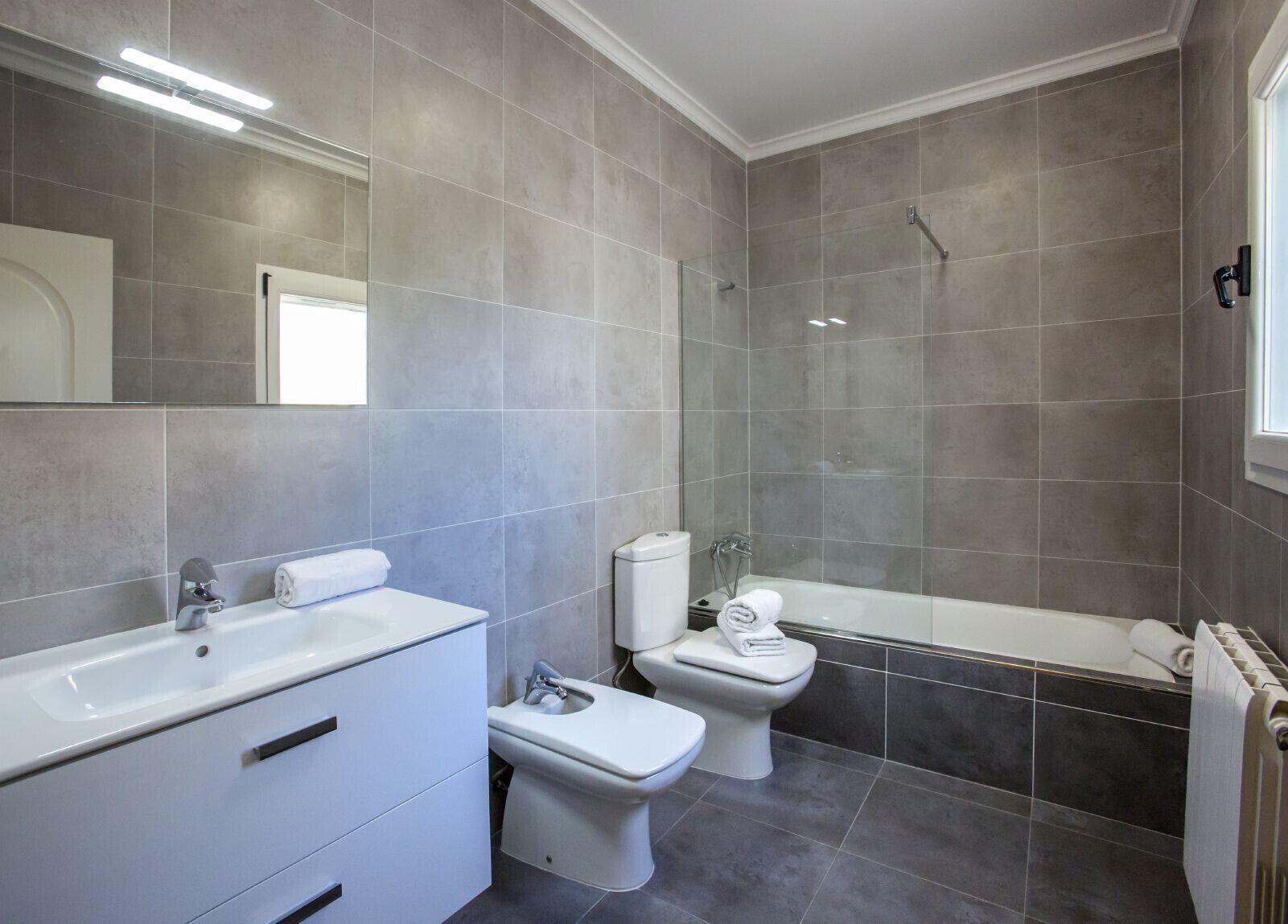 A modern bathroom with a bathtub, a sink, and two toilets.
