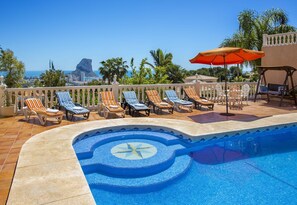 A poolside area with lounge chairs and an umbrella, overlooking a scenic view.