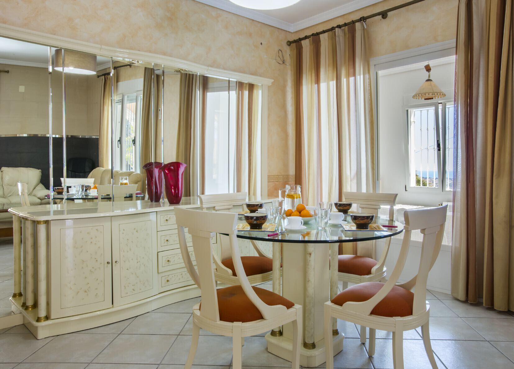 A dining area with a round glass table, white chairs, and a central island with a marble countertop.