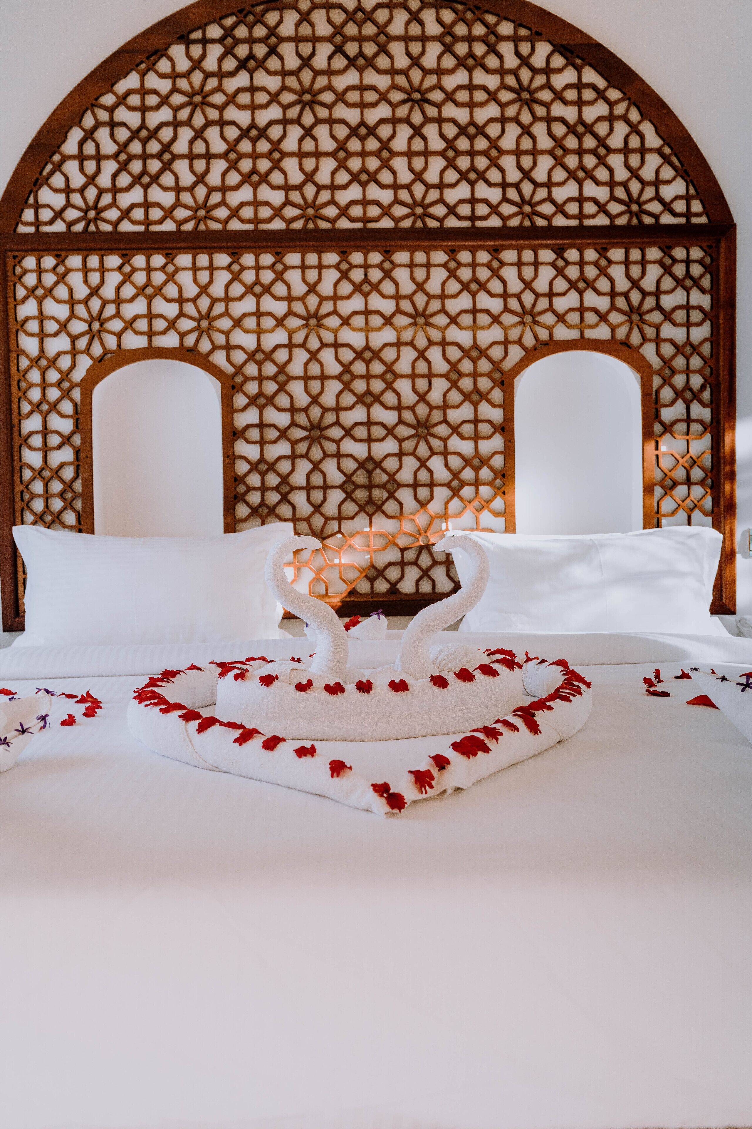 A bed with white linens and a decorative swan centerpiece, set against a patterned wooden headboard.