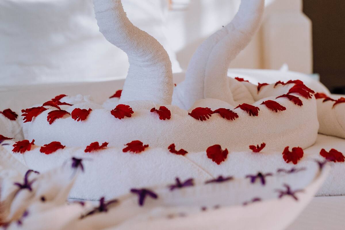 Una cama con ropa blanca y estampados florales rojos, una pared de celosía de madera y una pared blanca al fondo.