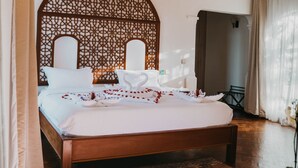 A bedroom with a large bed, a wooden headboard, a patterned rug, and a small table. - Saab Royale Resort (Ilyagaleni)