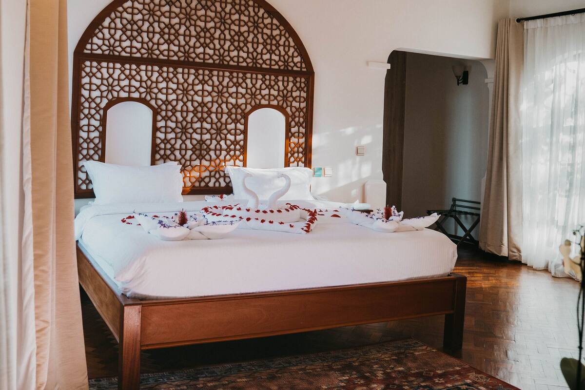 Un dormitorio con una cama grande, un cabecero de madera, un tapete estampado y una mesita.