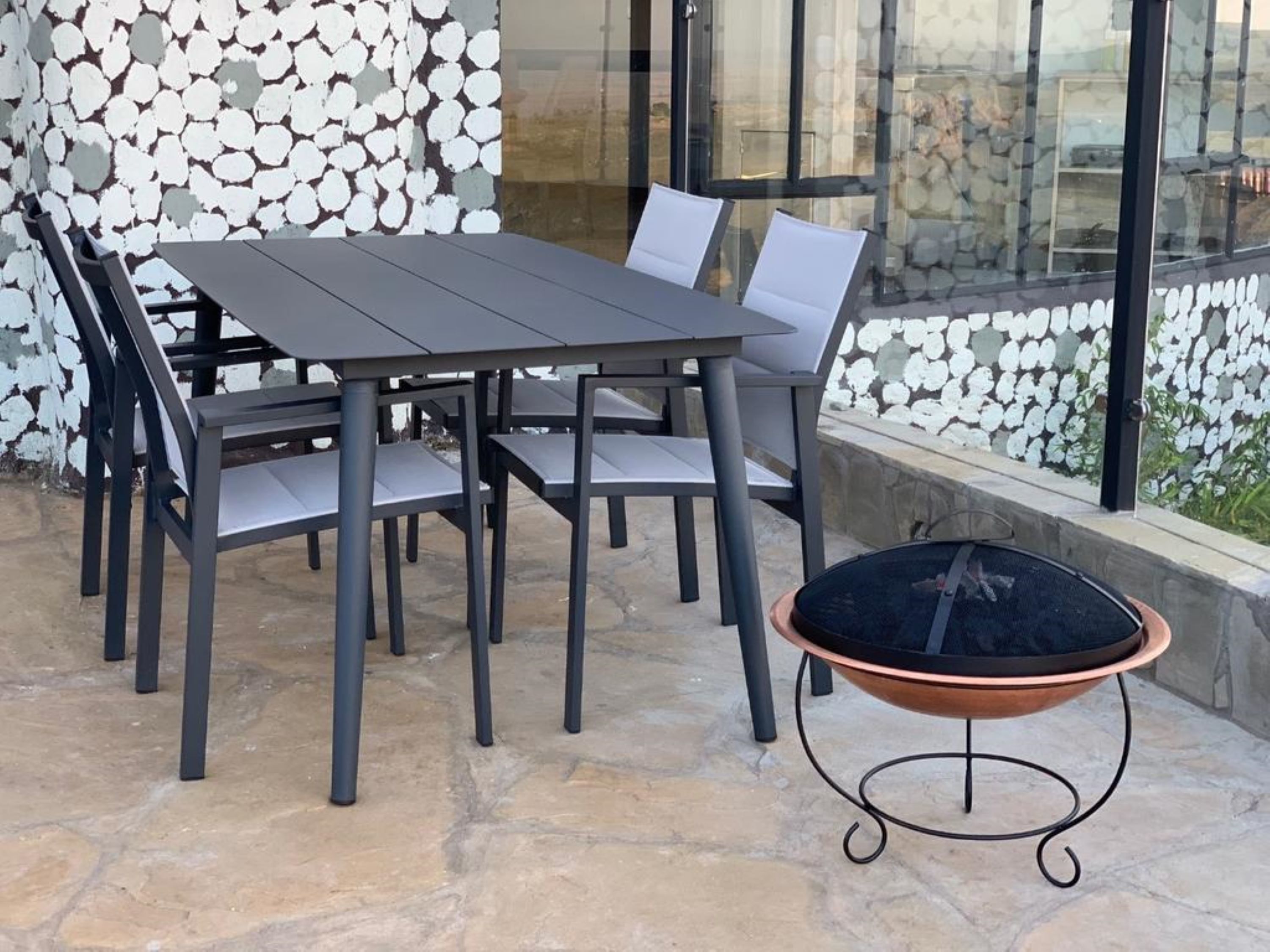 A patio area with a table and chairs, a glass wall, and a stone wall.