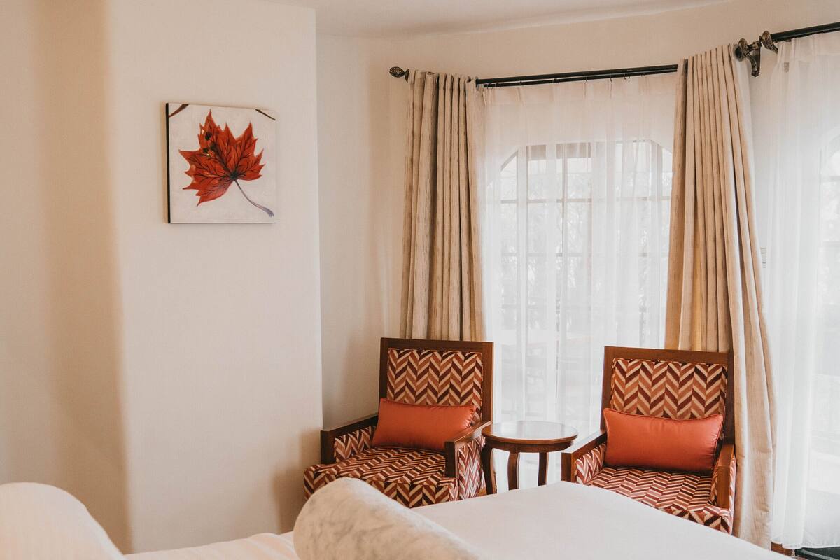 Una habitación de hotel con cama, dos sillones, una mesita y una ventana con cortinas.