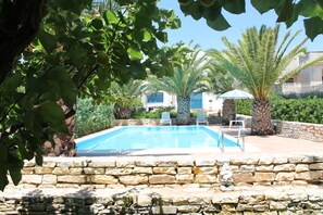 Una piscina con muros de piedra, rodeada de palmeras y un muro de piedra.