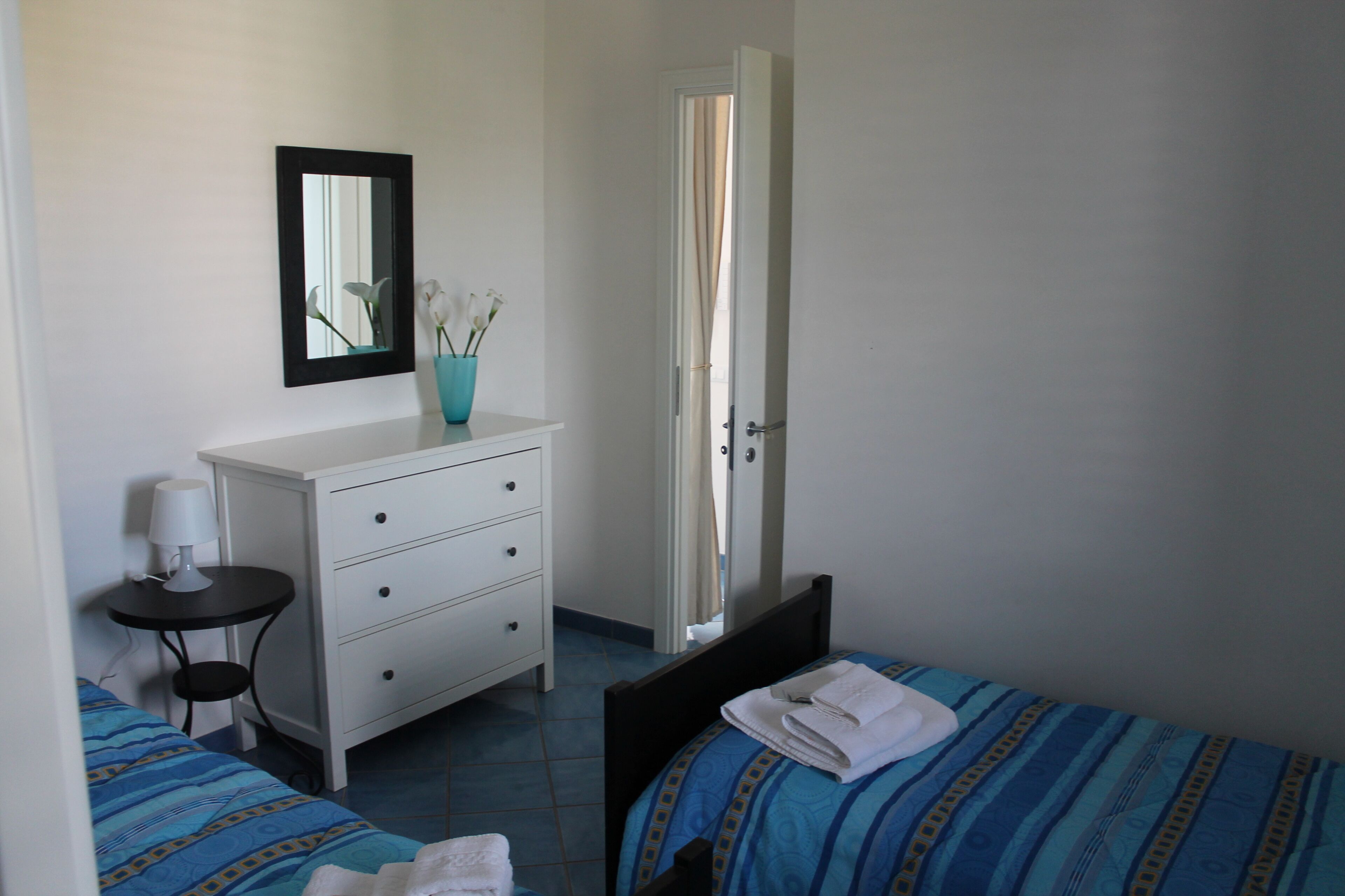 Une chambre avec deux lits, une commode, un miroir et une petite table avec une lampe.