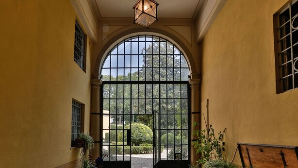 An arched entrance with a metal gate, potted plants, and a hanging light fixture. - CASA BEATRICE, Apartment with Private Garden inside the Walls of Lucca (Lucca)