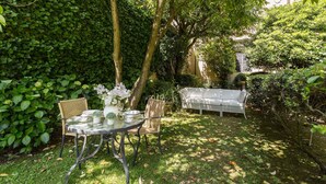 A garden with a round table and chairs, surrounded by lush greenery and a white sofa. - CASA BEATRICE, Apartment with Private Garden inside the Walls of Lucca (Lucca)