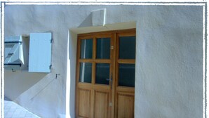 A wooden door with glass panels, a small potted plant, and a white wall with a light switch. - Village Studio Apartment (Sablet)