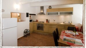 A compact kitchen with a refrigerator, microwave, stove, and wooden cabinets. - Village Studio Apartment (Sablet)