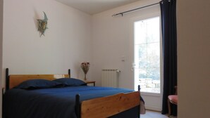 A bedroom with a wooden bed, a nightstand, a vase with flowers, a window with curtains, and a radiator.