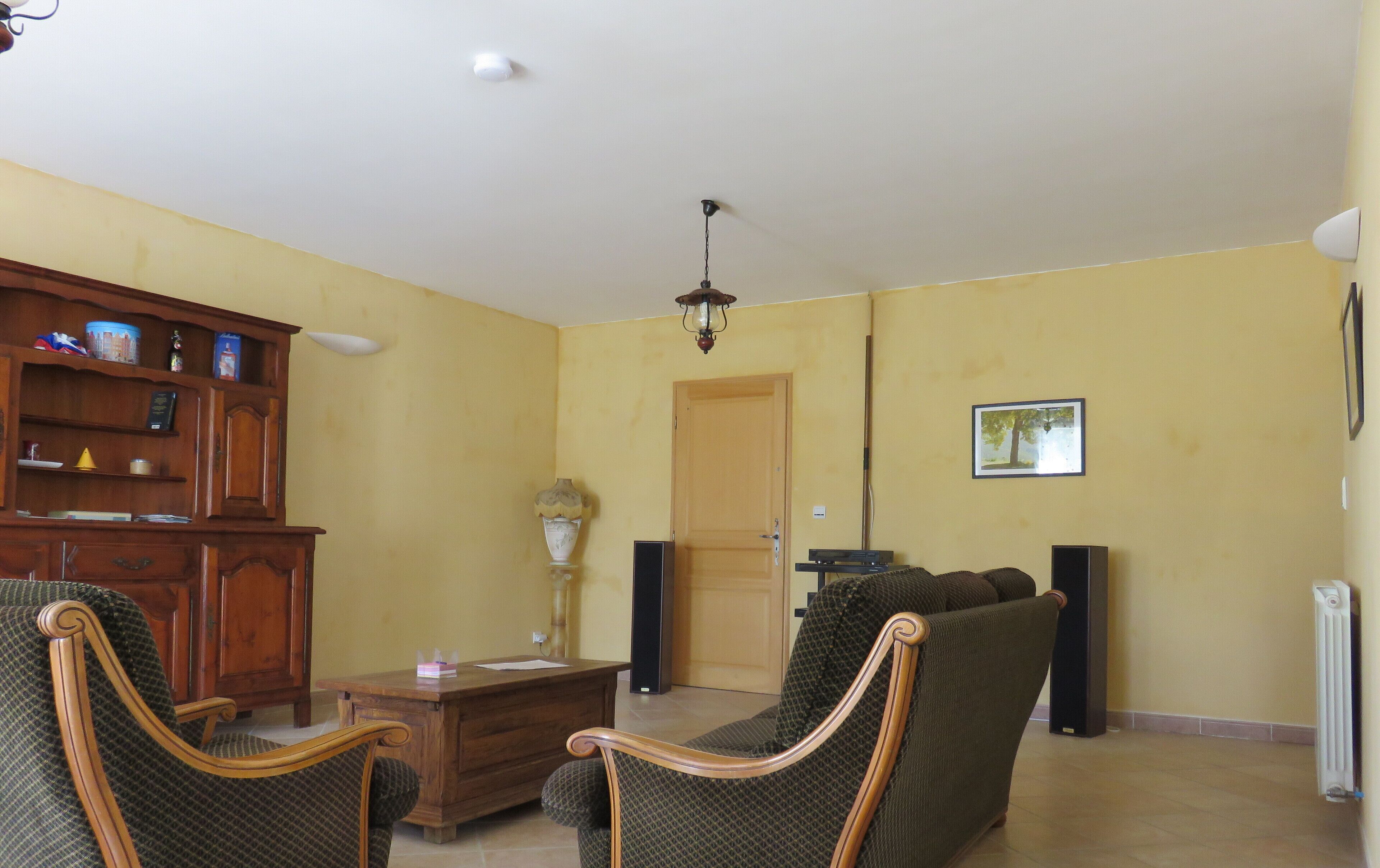A living room with a wooden cabinet, two armchairs, a coffee table, a lamp, a door, and a framed picture on the wall.