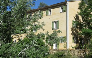 Un bâtiment à deux étages avec des volets verts, entouré d’arbres.