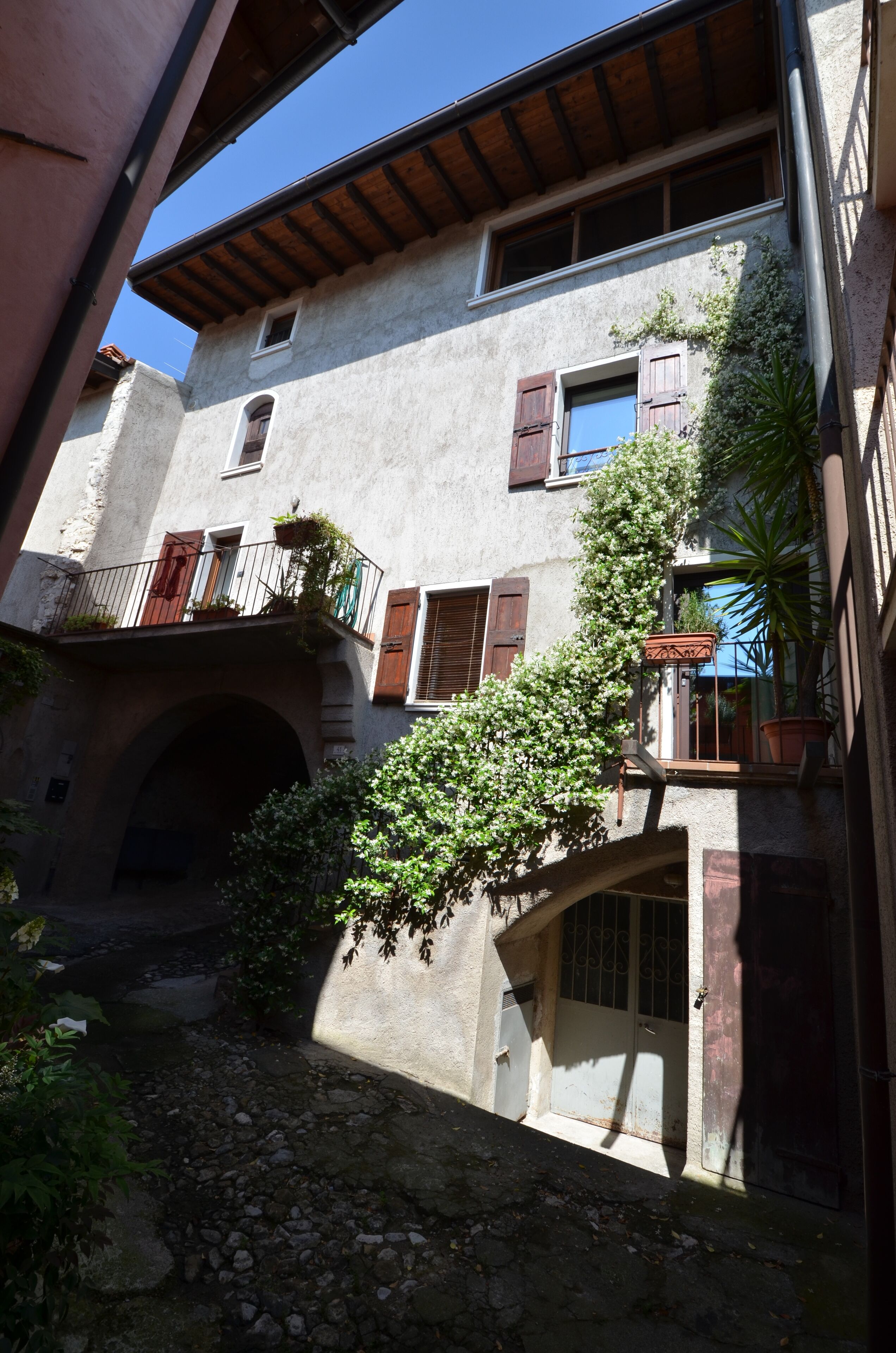 Un edificio rustico con un arco in pietra, balconi in legno e piante in vaso.