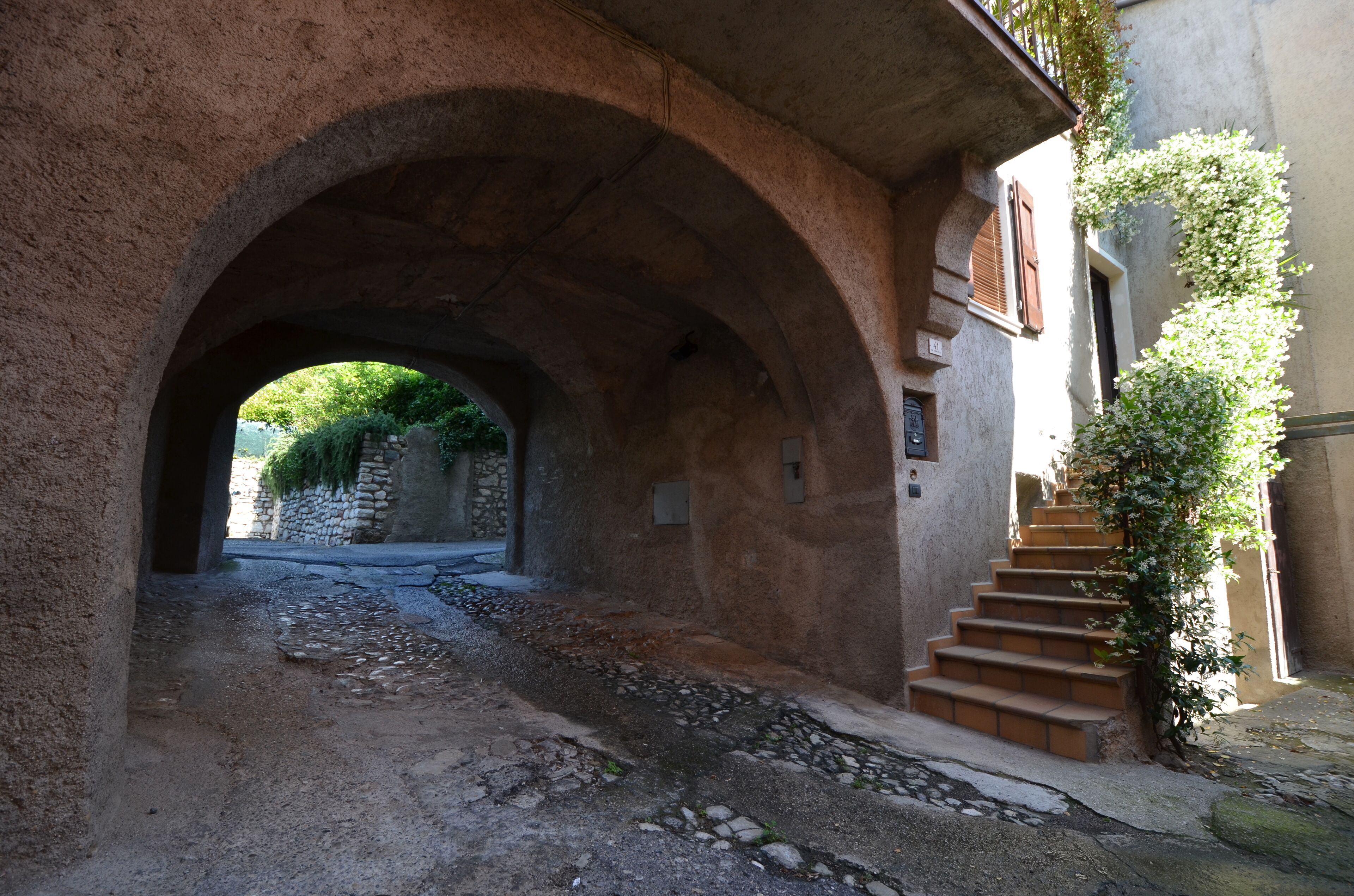 Eine gewölbte Steinbrücke, die zu einem Gebäude mit einer Treppe und einer mit Kletterpflanzen bewachsenen Mauer führt.
