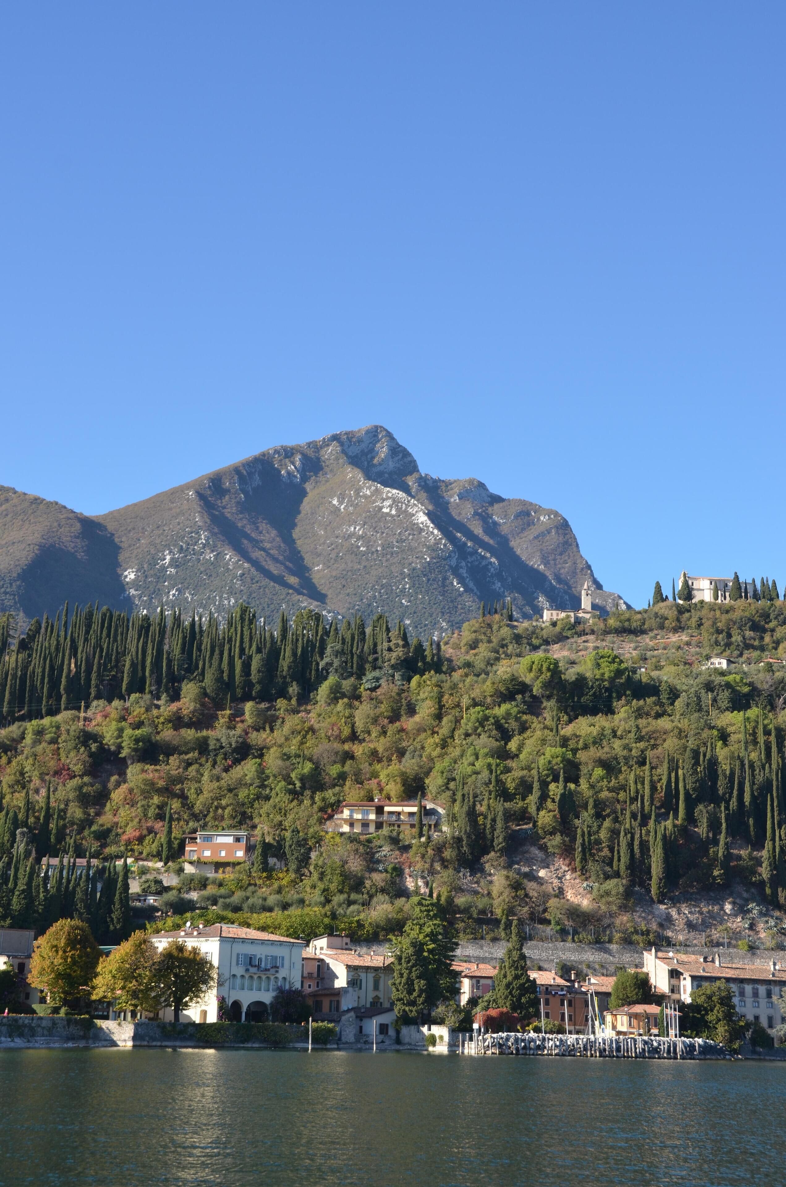 Un pueblo costero con edificios en una colina, un cielo azul despejado y una masa de agua al frente.