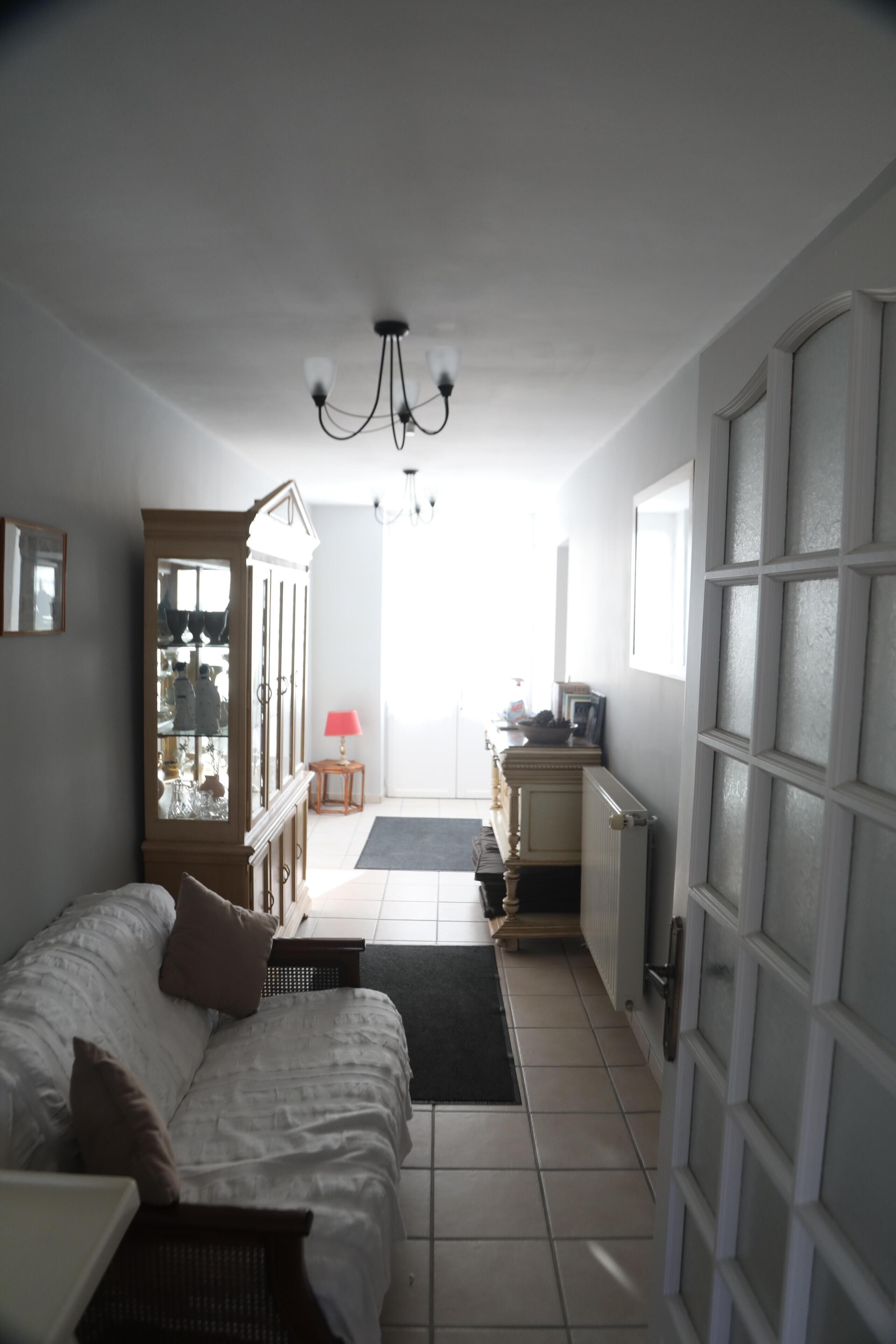 A hallway with a white sofa, a cabinet, a small table with a lamp, and a door leading to a kitchen area.