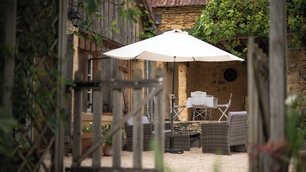 An outdoor seating area with wicker furniture, a table, and a white umbrella. - Gite au Manoir de Carlucet, 13th Century, between Sarlat and Montignac, Dordogne (Saint-Crepin-et-Carlucet)