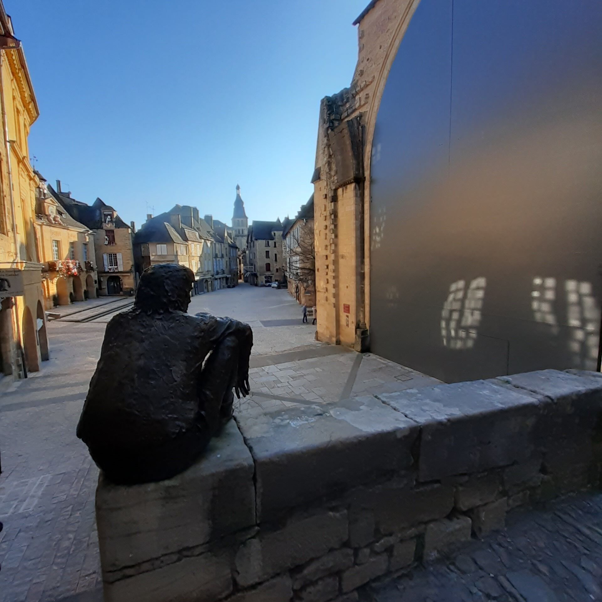 Eine Statue einer sitzenden Figur auf einem Steinsims mit Blick auf eine Straße mit historischen Gebäuden.