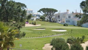 A golf course with sand bunkers, a well-maintained lawn, and surrounding buildings with white and blue exteriors.