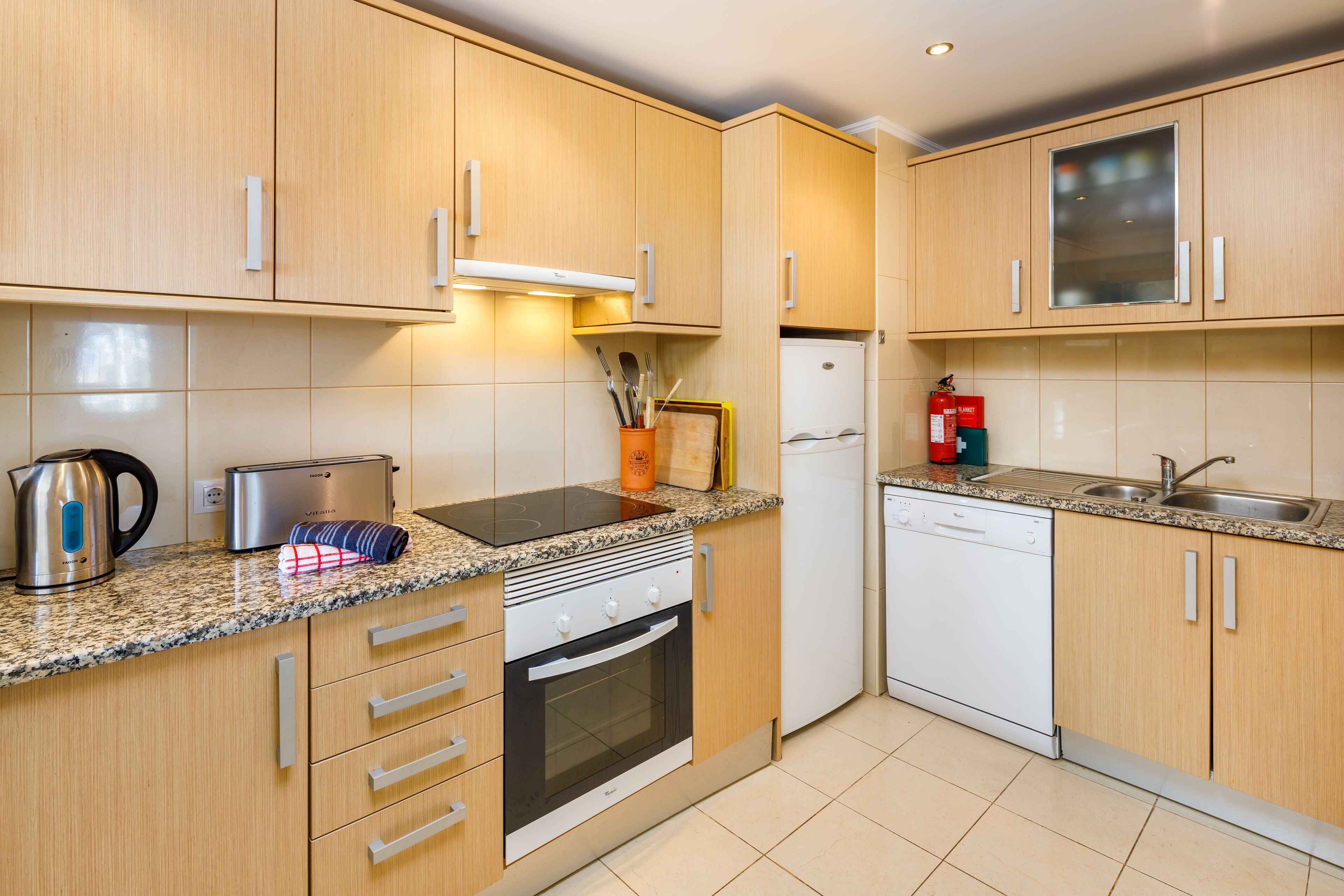 A modern kitchen with wooden cabinets, a built-in oven, a dishwasher, and a granite countertop.