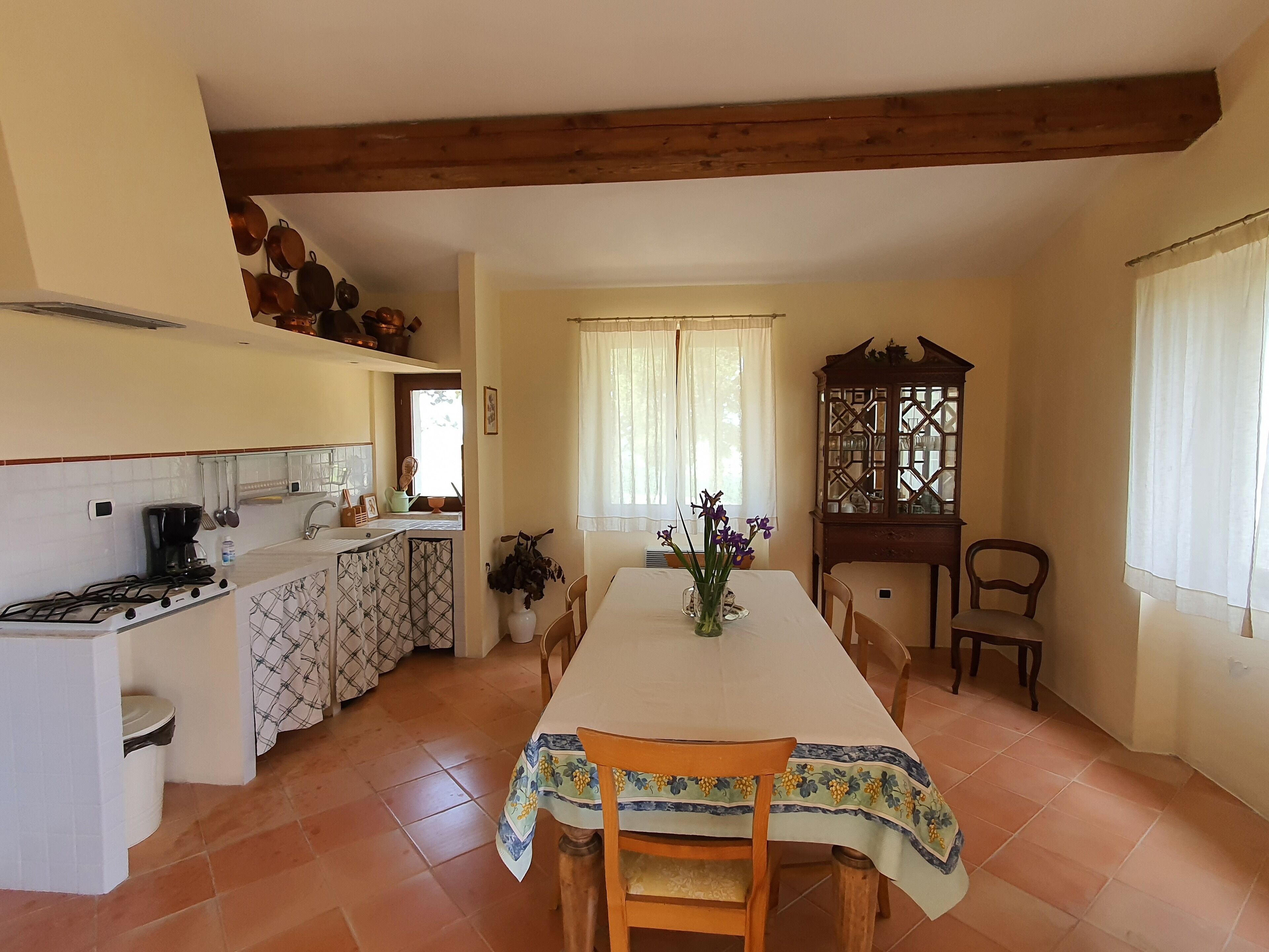 A kitchen with a dining area, featuring a tiled floor, a stove, a sink, and a table with chairs.
